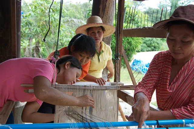 Women artisans learning and weaving handmade cotton textiles together at a community weaving workshop in northern Thailand.