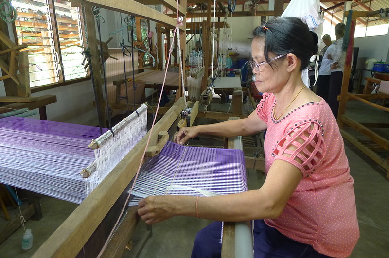 Thai artisan weaving hand-dyed purple cotton fabric on a traditional wooden loom at Fashion Accessories by Warm Heart.