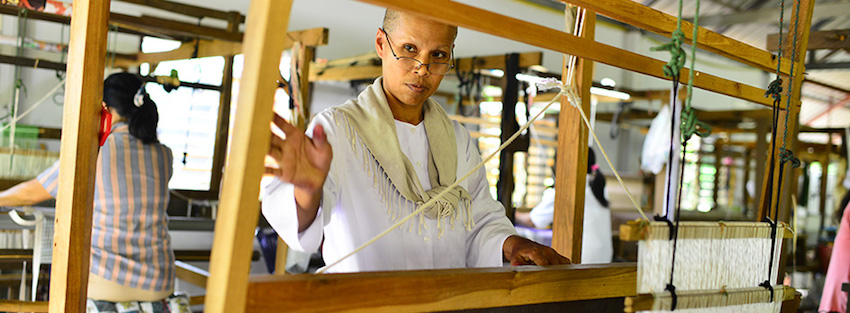 Woman artisan weaving handwoven cotton fabric on a traditional wooden loom at Fashion Accessories by Warm Heart in northern Thailand.