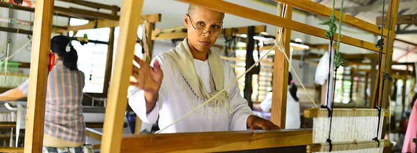 Woman artisan weaving handwoven cotton fabric on a traditional wooden loom at Fashion Accessories by Warm Heart in northern Thailand.